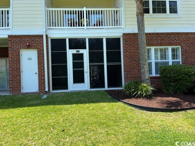 view of exterior entry with a balcony and a lawn