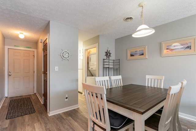 dining area featuring wood-type flooring, a textured ceiling, and stacked washer and dryer