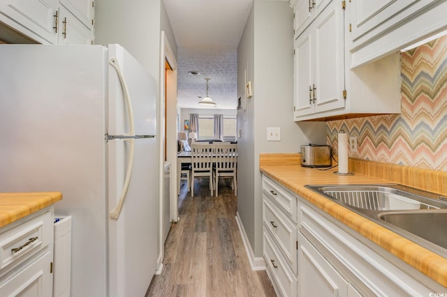 kitchen with white fridge, light hardwood / wood-style flooring, decorative light fixtures, and white cabinetry