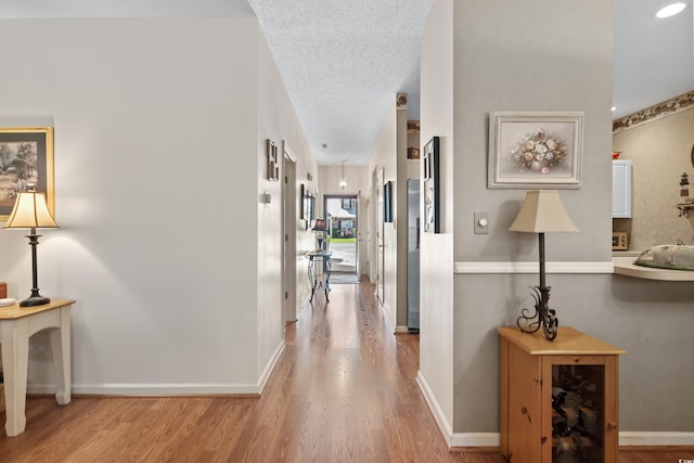 corridor with a textured ceiling and light hardwood / wood-style floors