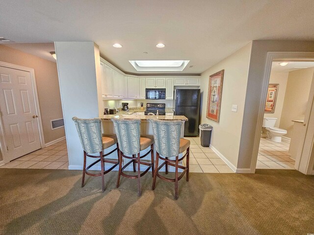 kitchen with light colored carpet, light stone countertops, black appliances, white cabinetry, and a kitchen breakfast bar