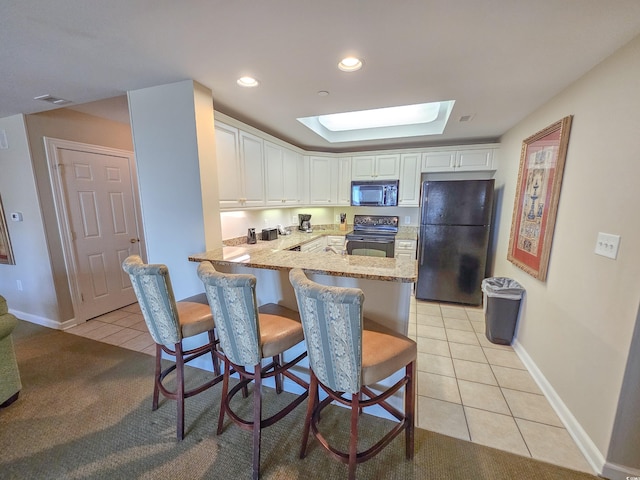 kitchen with light carpet, white cabinetry, black appliances, light stone counters, and a skylight