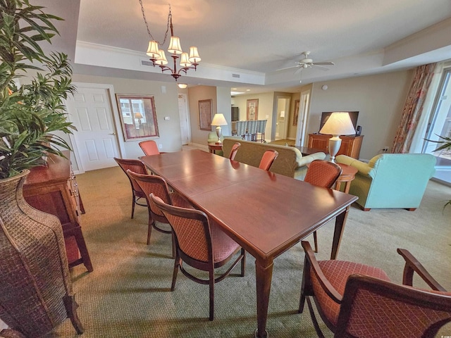 carpeted dining area featuring ceiling fan with notable chandelier and a tray ceiling