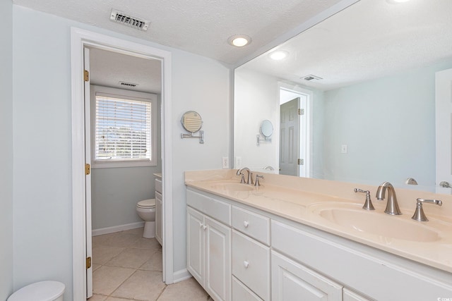 bathroom with tile flooring, double sink vanity, toilet, and a textured ceiling