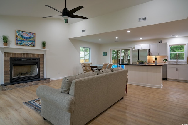 living room with ceiling fan, a brick fireplace, light hardwood / wood-style floors, and sink