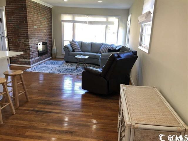 living room with a brick fireplace, a wealth of natural light, and dark wood-type flooring