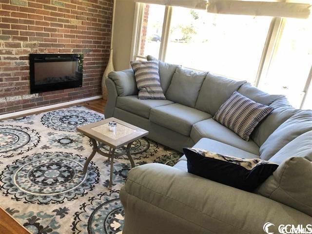 living room with a brick fireplace, brick wall, and hardwood / wood-style floors