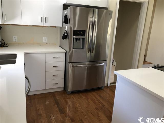 kitchen with dark hardwood / wood-style flooring, stainless steel fridge with ice dispenser, and white cabinetry