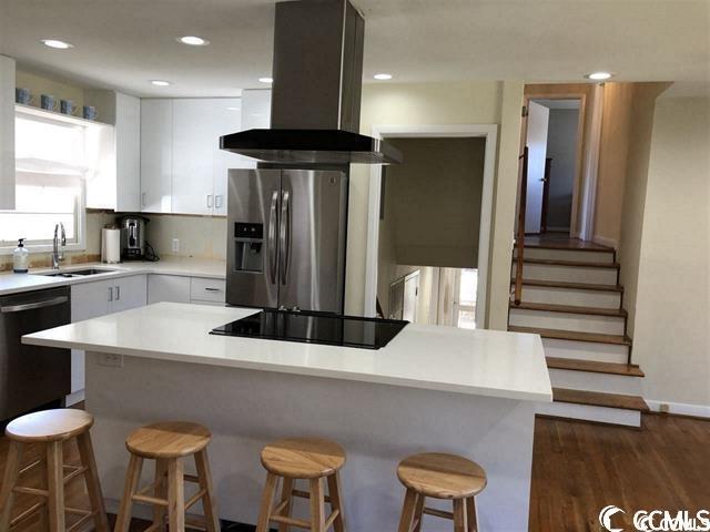 kitchen featuring white cabinets, black appliances, island range hood, and a breakfast bar area