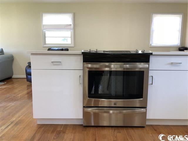 kitchen with plenty of natural light, stainless steel electric range, light hardwood / wood-style floors, and white cabinetry