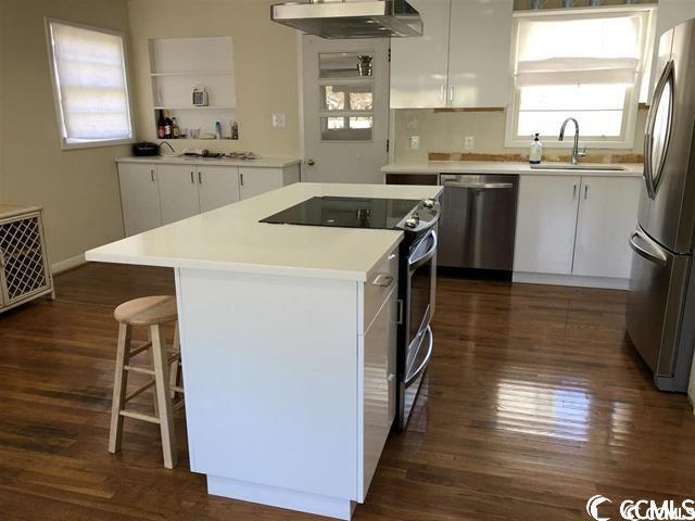 kitchen featuring a center island, sink, white cabinetry, stainless steel appliances, and extractor fan