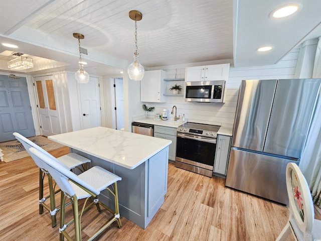 kitchen with light wood finished floors, a kitchen island, appliances with stainless steel finishes, and a breakfast bar