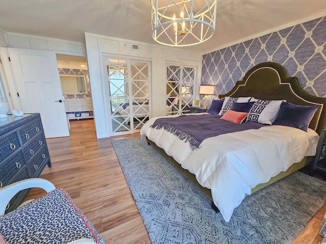 bedroom with visible vents, an inviting chandelier, a textured ceiling, wood finished floors, and wallpapered walls