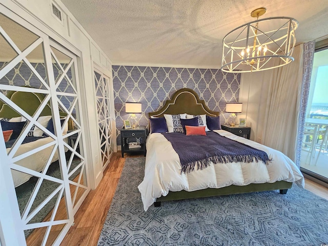 bedroom with a textured ceiling, an accent wall, wood finished floors, wallpapered walls, and an inviting chandelier