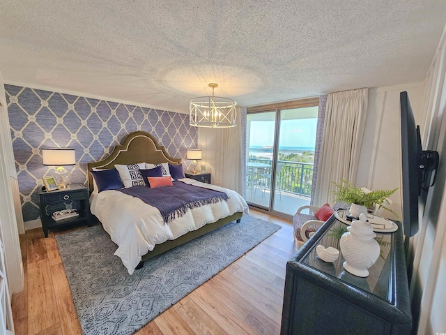 bedroom with access to exterior, a notable chandelier, light wood finished floors, a textured ceiling, and wallpapered walls