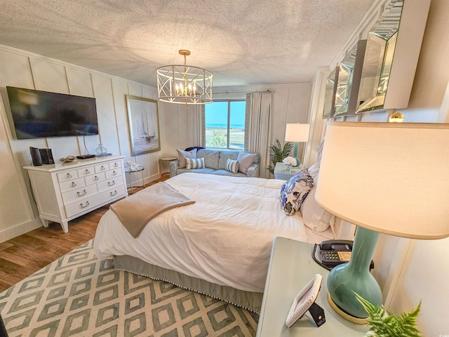 bedroom featuring a notable chandelier, a decorative wall, a textured ceiling, and wood finished floors