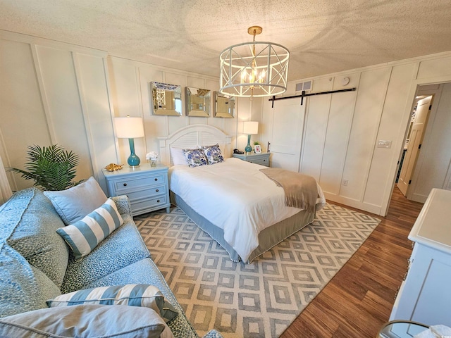 bedroom with visible vents, a decorative wall, a barn door, light wood-style floors, and a textured ceiling