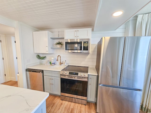 kitchen with light wood finished floors, light stone counters, appliances with stainless steel finishes, open shelves, and a sink