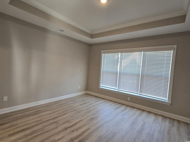 empty room with light hardwood / wood-style floors, a tray ceiling, and crown molding