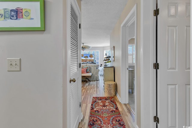 corridor with light wood-type flooring and a textured ceiling