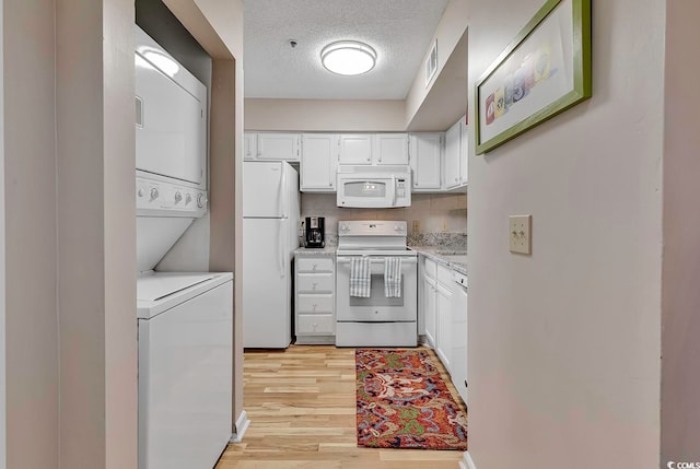 kitchen featuring white appliances, light hardwood / wood-style flooring, white cabinetry, stacked washer and dryer, and a textured ceiling