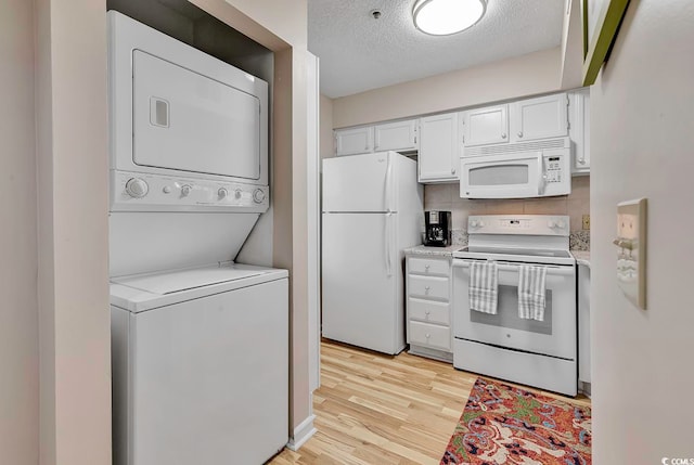 kitchen with white cabinets, white appliances, stacked washer / drying machine, light hardwood / wood-style floors, and a textured ceiling