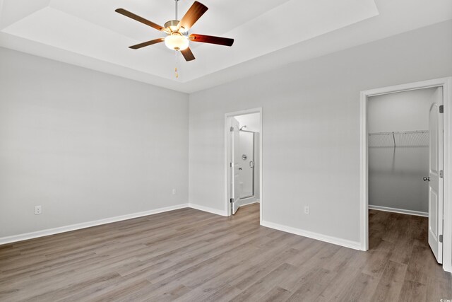 unfurnished bedroom with a walk in closet, baseboards, wood finished floors, a tray ceiling, and a closet