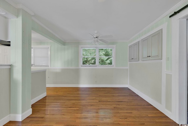 unfurnished room with ceiling fan, crown molding, hardwood / wood-style flooring, and a barn door