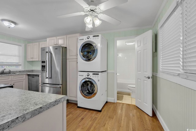 laundry room featuring crown molding, light hardwood / wood-style flooring, ceiling fan, and stacked washer / drying machine