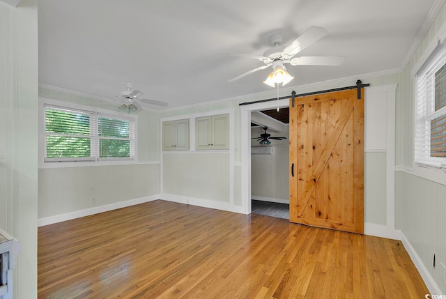 unfurnished bedroom featuring ornamental molding, ceiling fan, light hardwood / wood-style floors, and a barn door