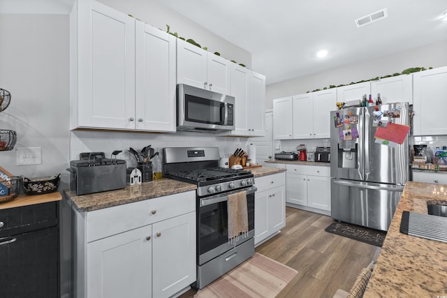 kitchen with decorative backsplash, white cabinetry, dark wood-type flooring, and appliances with stainless steel finishes