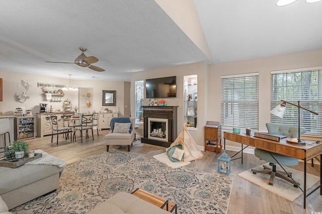 living area with baseboards, wood finished floors, a textured ceiling, a fireplace, and ceiling fan with notable chandelier