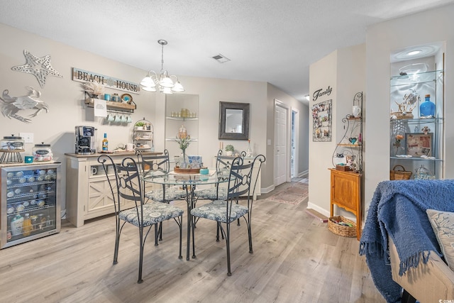 dining room featuring a notable chandelier, light wood finished floors, visible vents, a textured ceiling, and beverage cooler