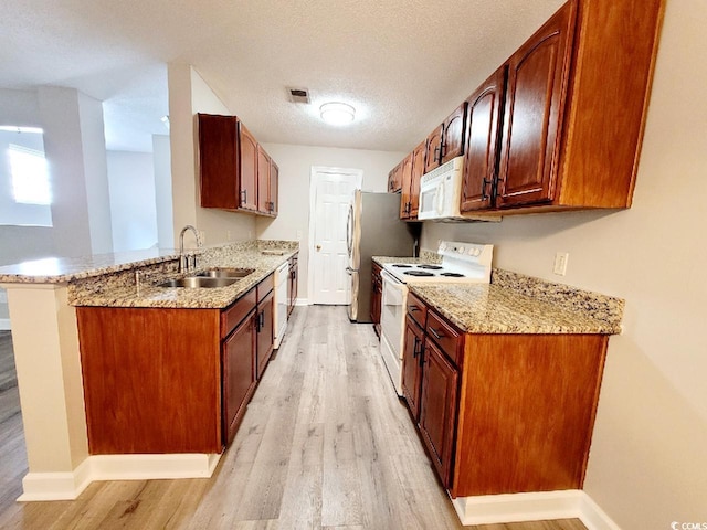 kitchen with a sink, a textured ceiling, light stone countertops, light wood-type flooring, and white appliances