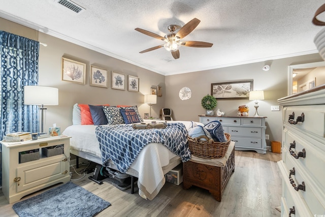 bedroom featuring a textured ceiling, ornamental molding, light wood-type flooring, and visible vents