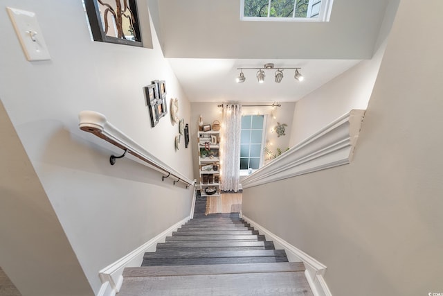 staircase with rail lighting, baseboards, and wood finished floors