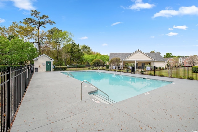 pool with a patio area, fence, and an outbuilding