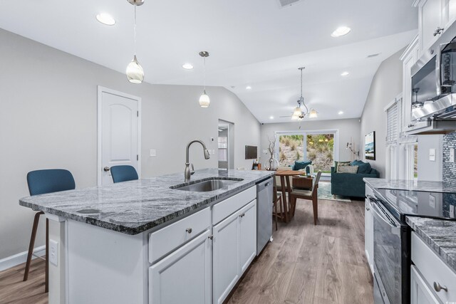 kitchen with an island with sink, sink, white cabinets, a kitchen breakfast bar, and hanging light fixtures