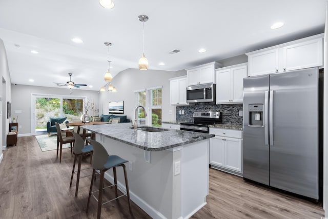 kitchen with stone counters, appliances with stainless steel finishes, sink, white cabinets, and a center island with sink