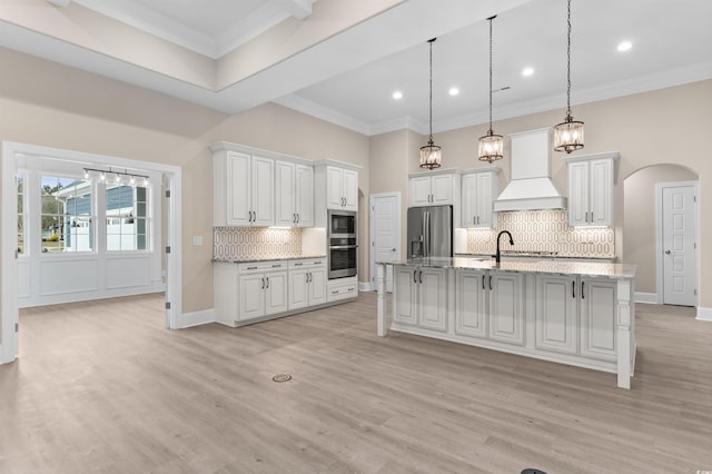 kitchen with appliances with stainless steel finishes, premium range hood, hanging light fixtures, white cabinets, and backsplash