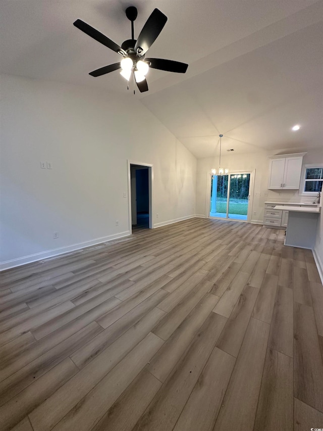 unfurnished living room featuring vaulted ceiling, light hardwood / wood-style floors, and ceiling fan with notable chandelier