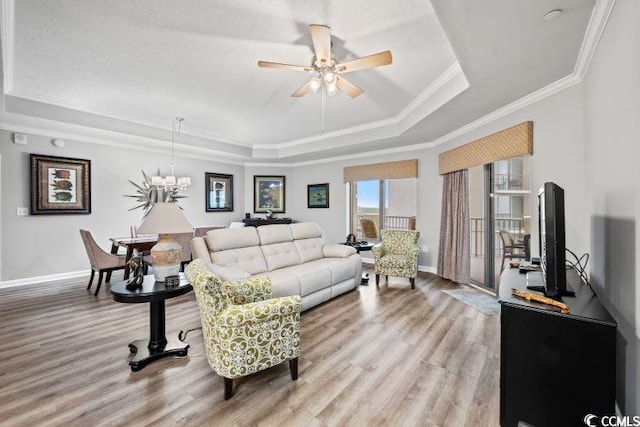 living room with ornamental molding, light hardwood / wood-style flooring, ceiling fan with notable chandelier, and a raised ceiling