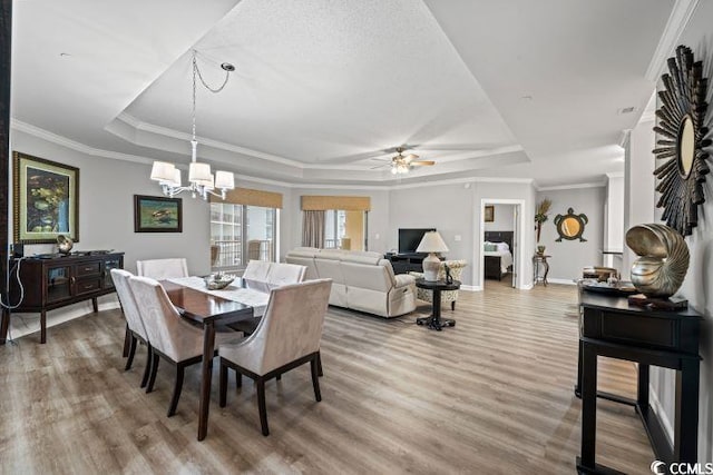 dining area with hardwood / wood-style flooring, ornamental molding, ceiling fan with notable chandelier, and a tray ceiling