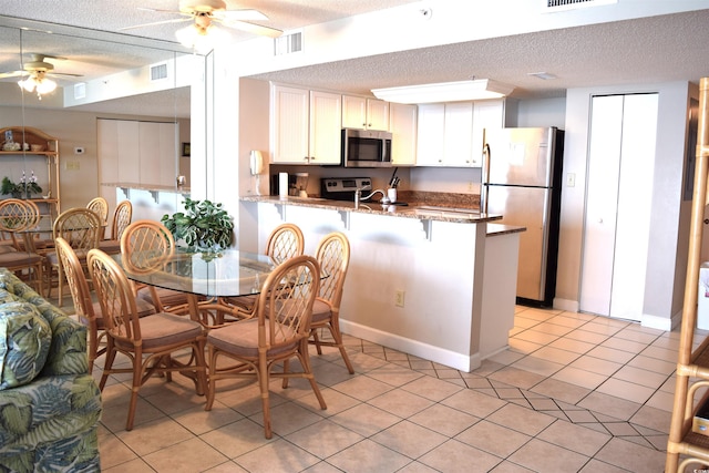 kitchen with stainless steel appliances, kitchen peninsula, dark stone counters, a textured ceiling, and white cabinets