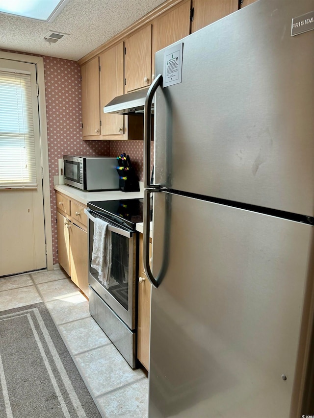 kitchen with light brown cabinets, light tile floors, stainless steel appliances, and a textured ceiling