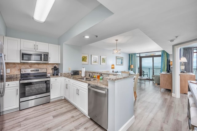 kitchen featuring kitchen peninsula, white cabinetry, light stone countertops, light wood-type flooring, and appliances with stainless steel finishes