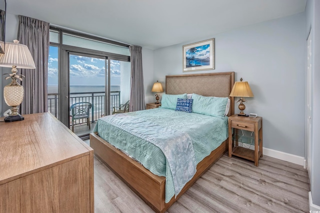 bedroom featuring a water view, light hardwood / wood-style floors, and access to exterior