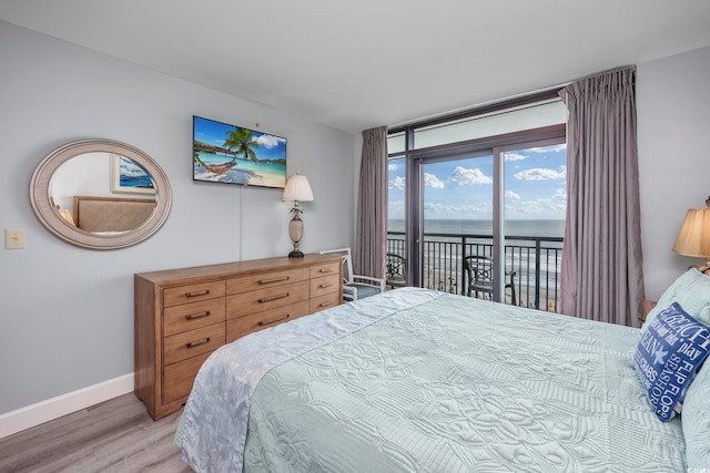 bedroom with hardwood / wood-style floors, a water view, and access to exterior