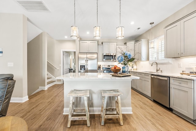 kitchen with decorative light fixtures, light wood-type flooring, backsplash, stainless steel appliances, and sink