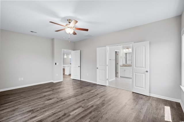 unfurnished bedroom featuring connected bathroom, dark wood-type flooring, and ceiling fan